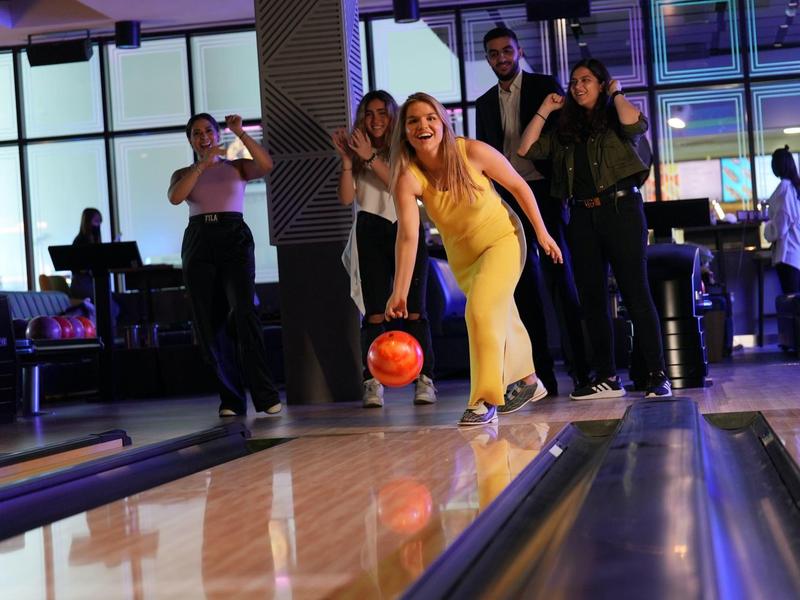 Lidé si užívají bowling v moderní, dobře osvětlené bowlingové hale.