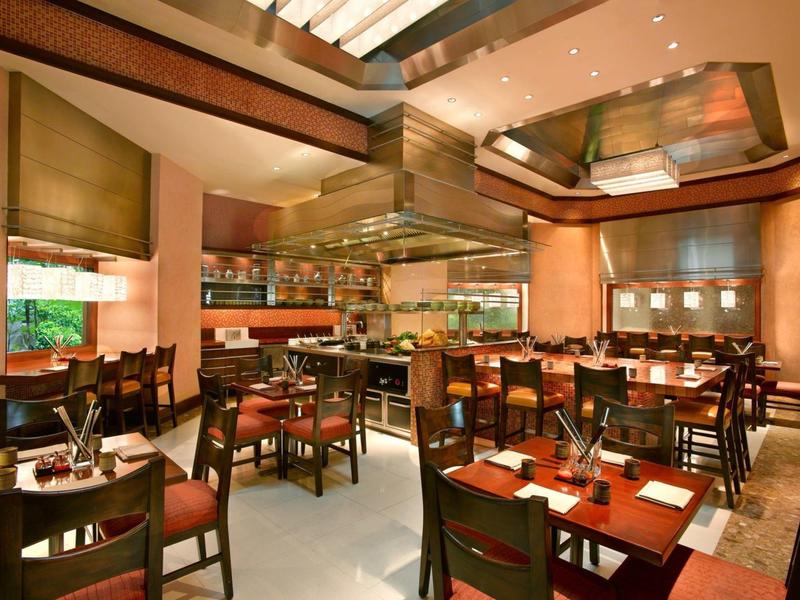 Moderní restaurace s dřevěnou výzdobou, několika stoly a centrální jídelní částí.