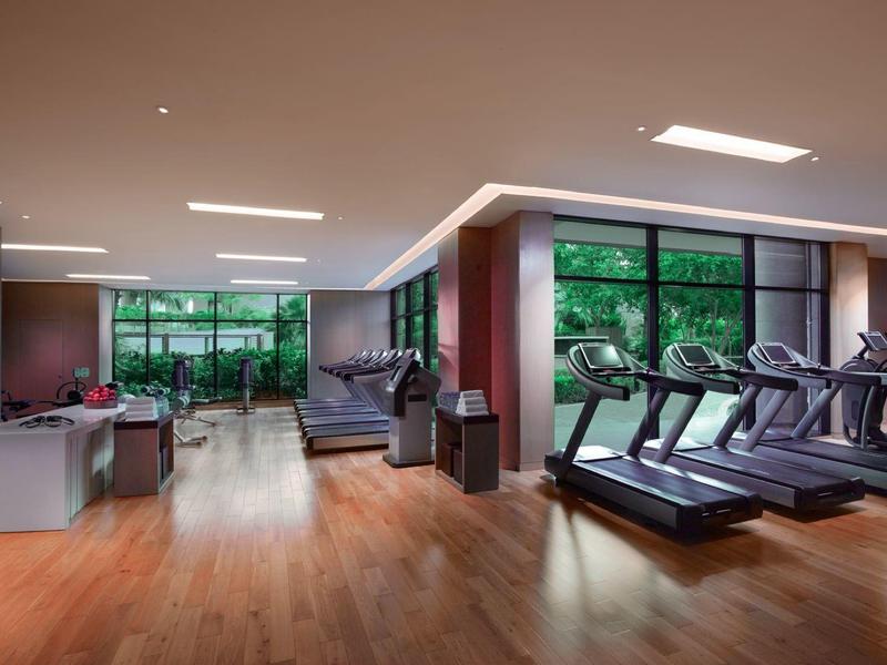 Světle posilovna s běžeckými pásy, činkami a velkými okny s výhledem do zeleně.