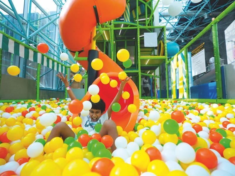 Dítě si hraje v barevném bazénu s míčky s oranžovo-žlutou skluzavkou uvnitř.