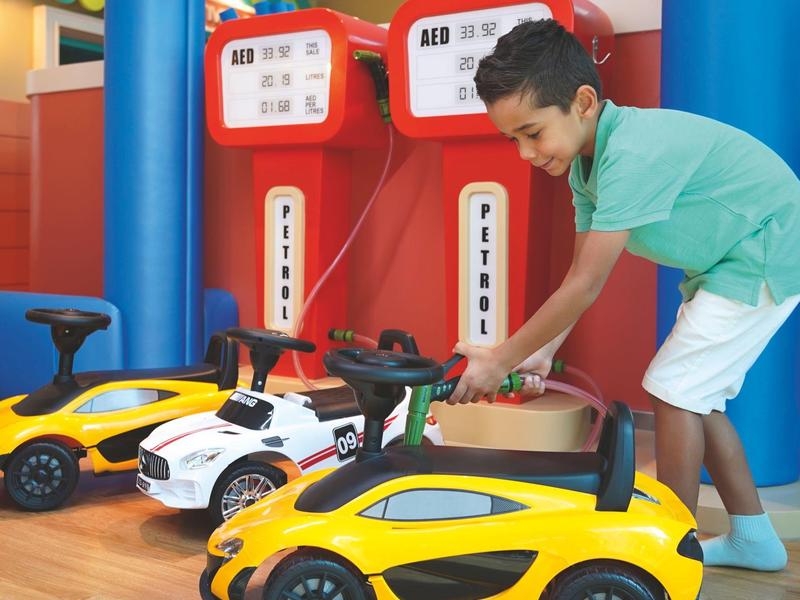 Chlapec si hraje se žlutými a bílými autíčky v barevném vnitřním prostoru.