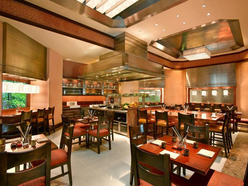 Velká hotelová vstupní hala s bujnou zelení a moderními zavěšenými dřevěnými sochami.