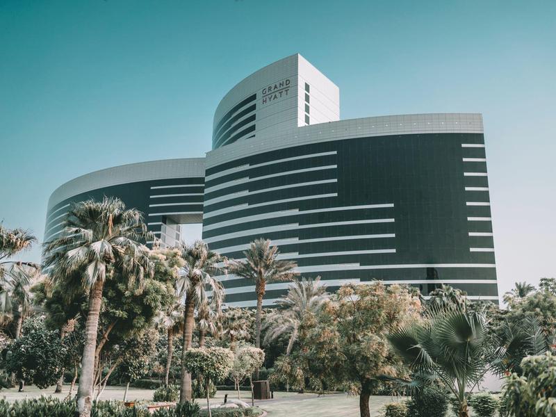 Moderní zakřivená budova hotelu s palmami a jasnou oblohou v pozadí.