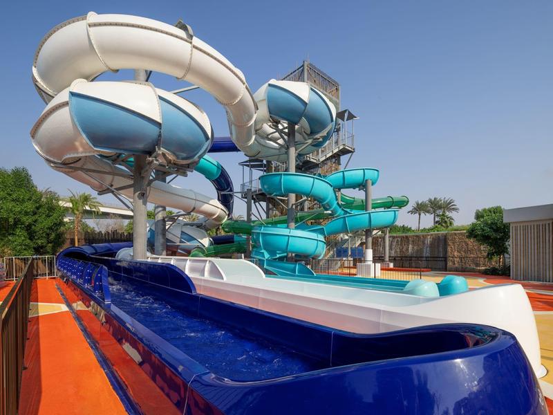 Vodní park s barevnými trubkovými skluzavkami a jasnou oblohou v slunečný den.