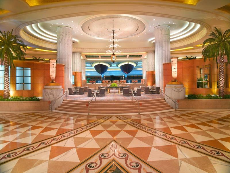 Elegantní hotelová hala s kolonádami, tropickými rostlinami a geometrickou mramorovou podlahou.