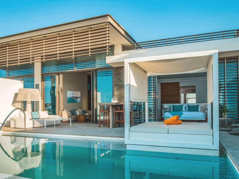 Modern hotel pool with daybed and glass facade under clear sky
