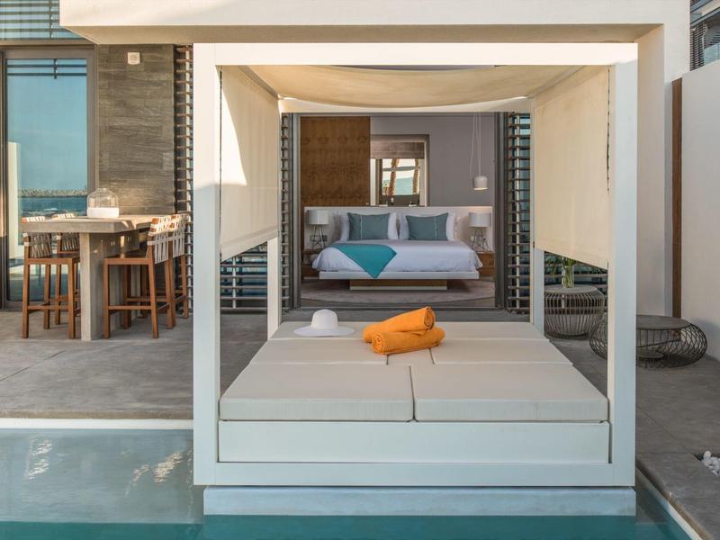 Modern canopy double bed and pool in front of a hotel room with dining table.