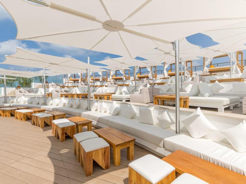 Elegant outdoor lounge with white cushions, wooden tables, and sun umbrellas, perfect for relaxing.