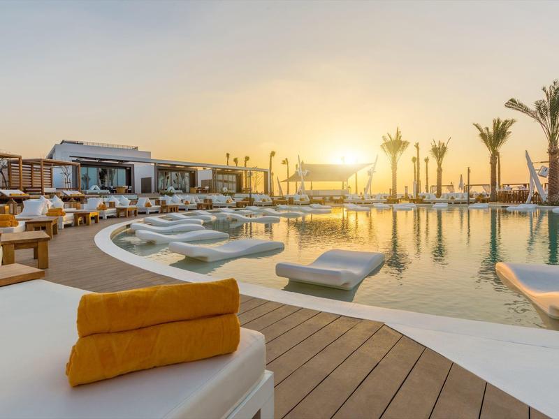 Luxury hotel pool with sun loungers and palm trees at sunset.