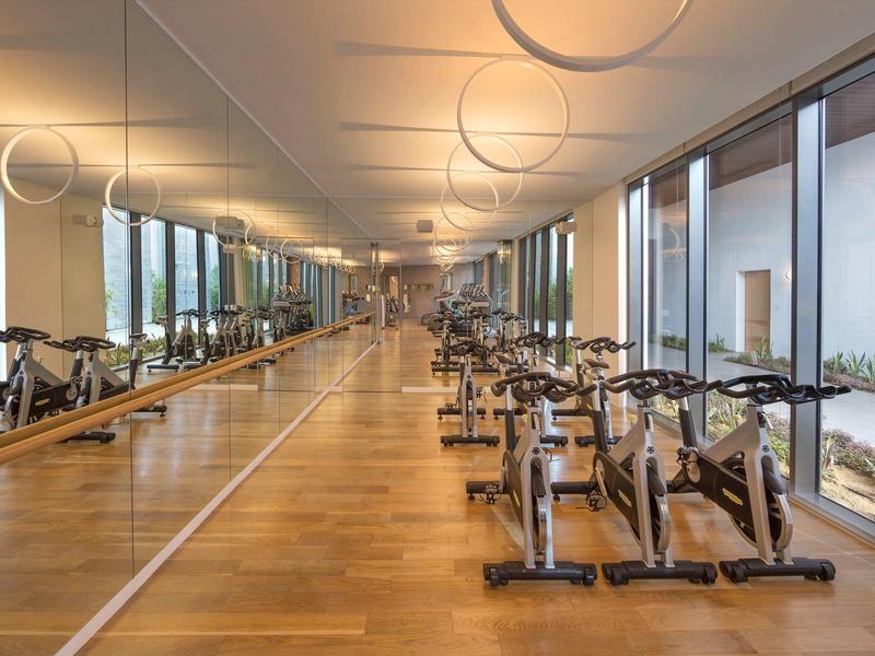 Modern gym with wood flooring, multiple exercise bikes, and floor-to-ceiling windows.