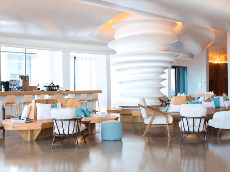 Bright, modern restaurant with large windows, white furniture, and wooden chairs.