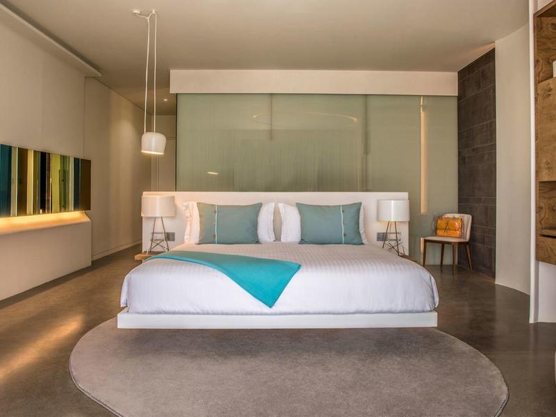 Modern hotel room with large bed and minimalist design in neutral tones.