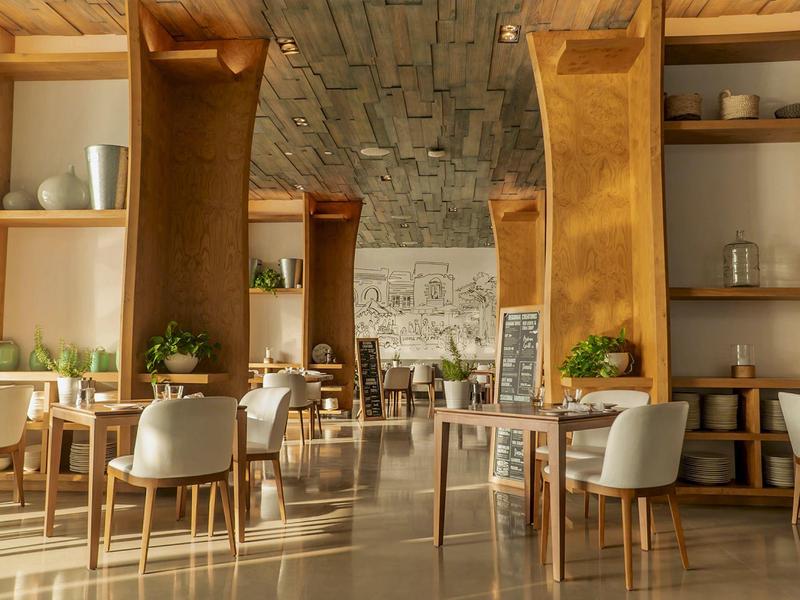 Bright restaurant with wooden furniture, white chairs, and plants on tables.