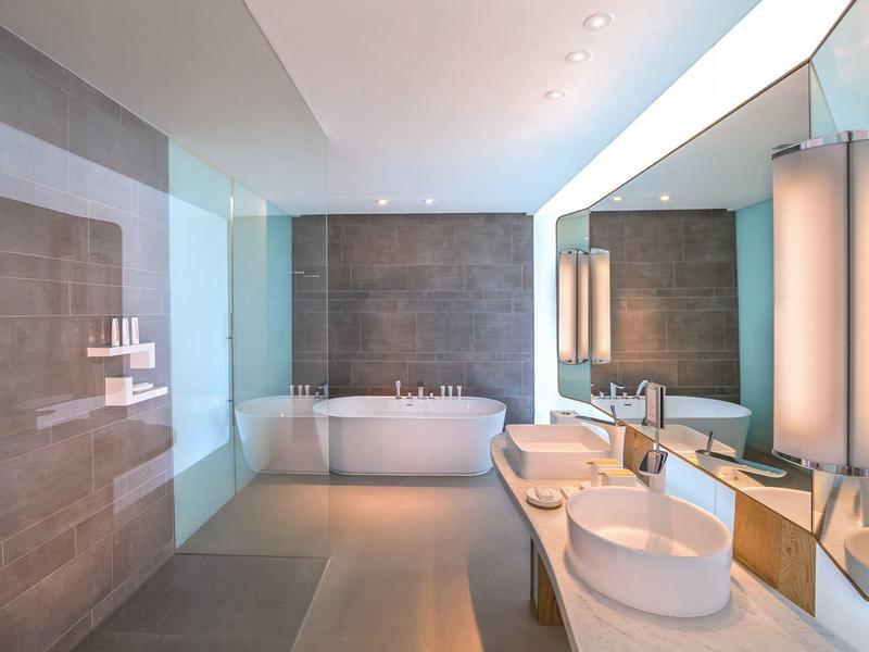 Modern bathroom with freestanding bathtub, two sinks, and illuminated mirror.