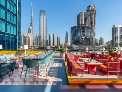 Moderne Dachterrasse mit bunten Sitzgruppen, Tischen und Blick auf Wolkenkratzer in der Stadt.