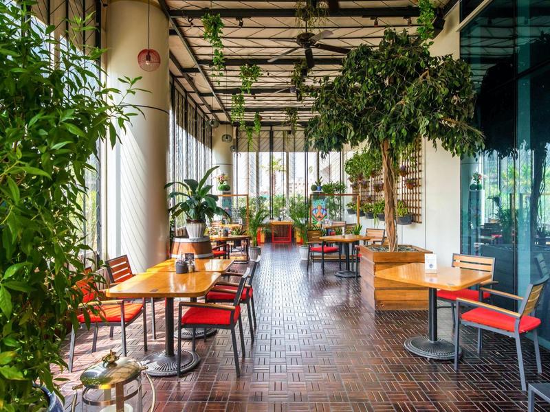 Gezellig hotelterras met houten tafels, rode stoelen en veel groene planten.