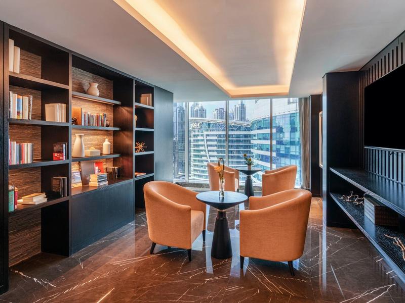 Moderne lounge met leren stoelen, ronde tafel, boekenkasten en groot raam met uitzicht op de stad.