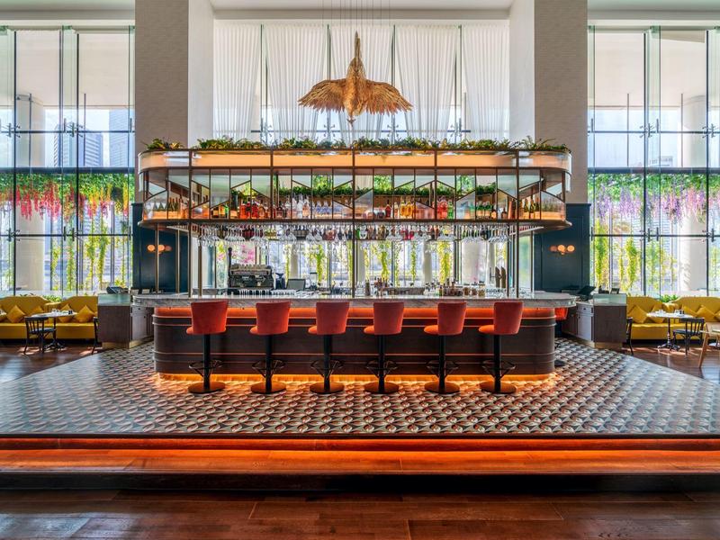 Elegante hotelbar met rode krukken, geometrische vloertegels en grote ramen met natuurlijk licht.