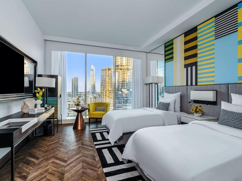 Modern hotelkamer met twee bedden, uitzicht op de stad, patroonmuur en houten vloer.