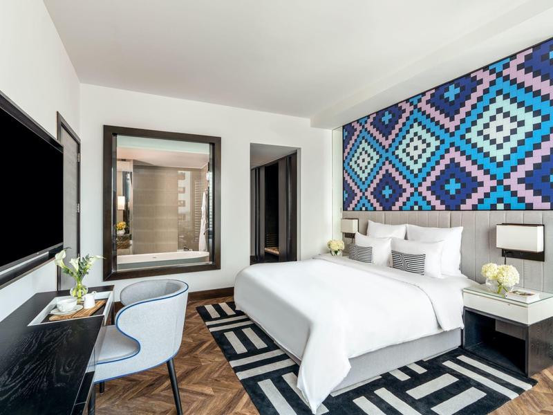 Moderne hotelkamer met queensize bed, geometrische muurkunst, bureau, stoel en zwart-witte vloerkleed.