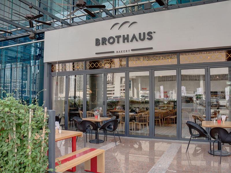 Modern restaurant met glazen gevel, buitenzitplaatsen en planten in een lichte ruimte.