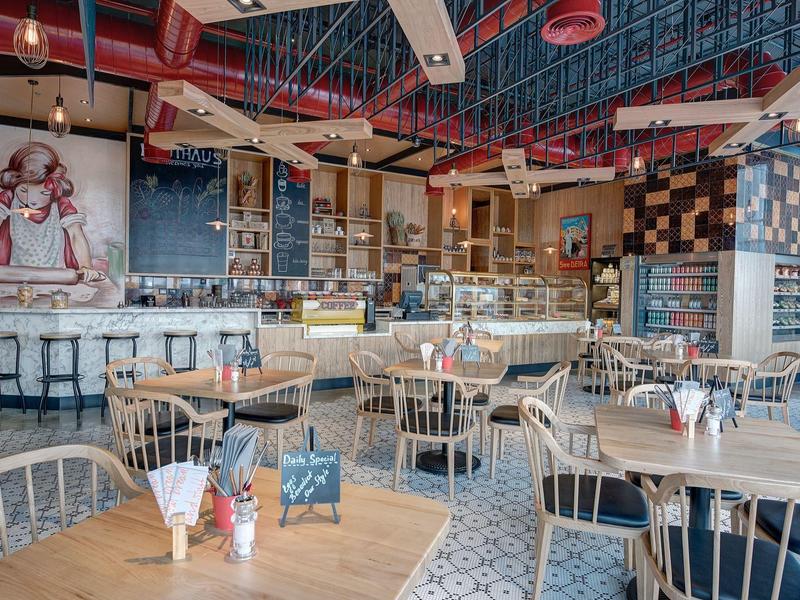 Ruim modern restaurant met houten tafels, metalen stoelen en een muurschildering aan de muur.