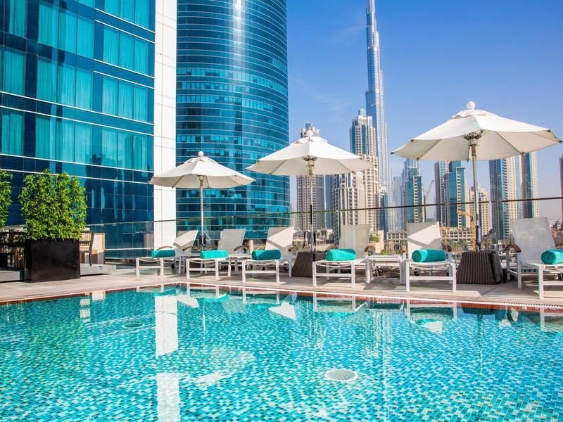 Modern hotel dakterras zwembad met ligstoelen en parasols tegen stadswolkenkrabbers.