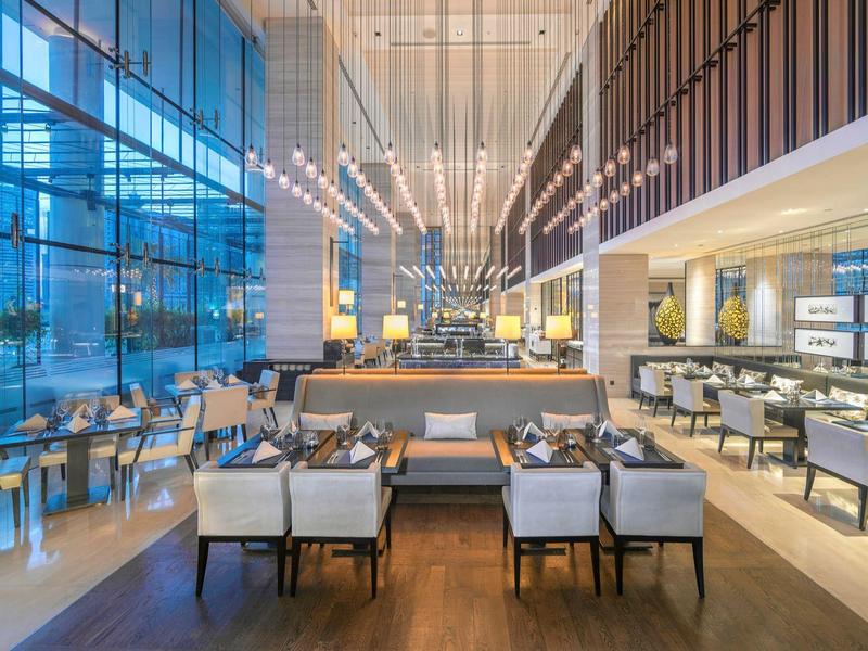 Ruime hotel lobby met moderne zitgelegenheid, hoog plafond en grote glazen ramen voor veel natuurlijk licht.