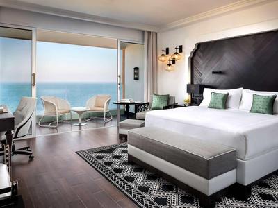 Modernes Hotelzimmer mit großem Bett, Sitzbereich und Meerblick durch bodentiefe Fenster.