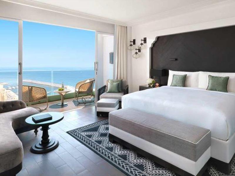 Helles Hotelzimmer mit großem Bett, Sitzbereich und Balkon mit Meerblick.