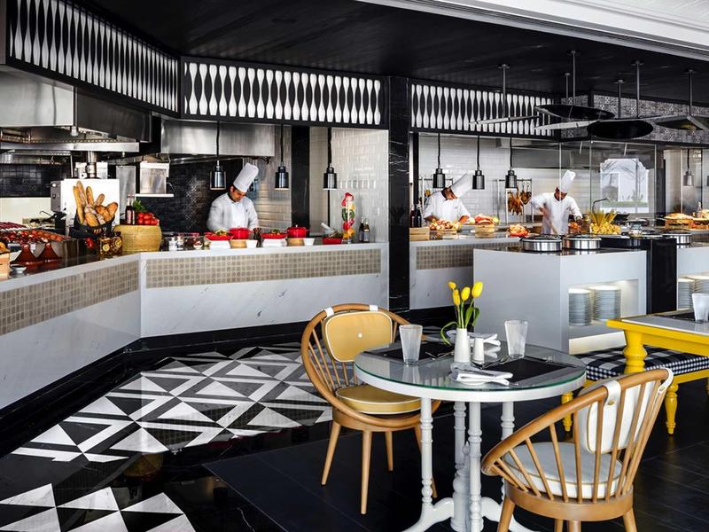Moderner Gastronomiebereich mit Holztischen, gelben Sitzbänken und gemustertem Schwarz-Weiß-Boden.