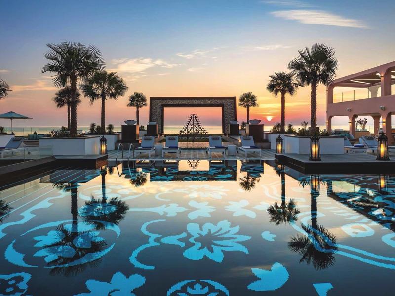 Moderner Pool mit Blumenmuster spiegelt Palmen und Abendhimmel in warmen Farben wider.