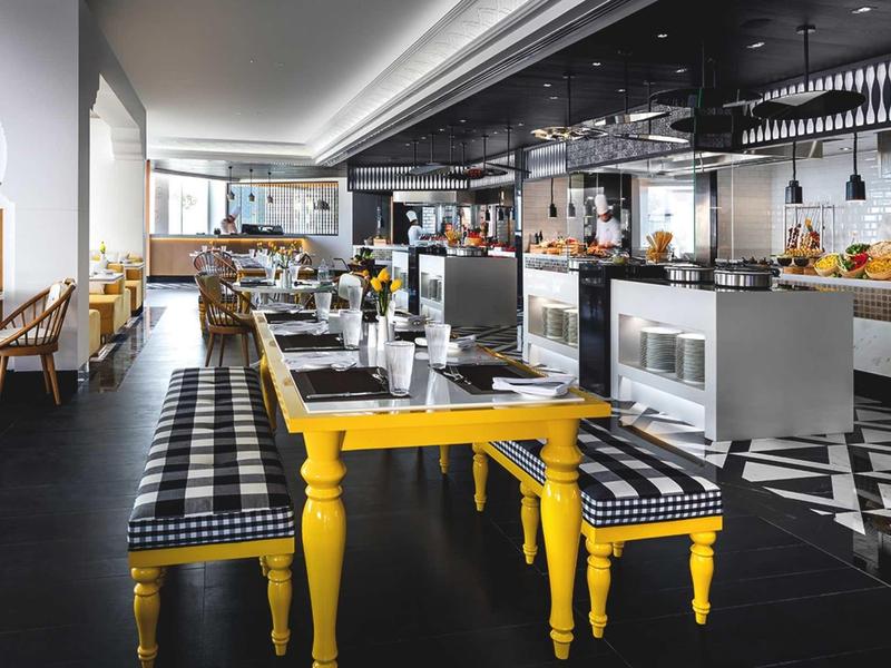 Moderner Restaurantinnenraum mit gelbem Tisch, karierten Sitzpolstern und geometrischem Bodenmuster.