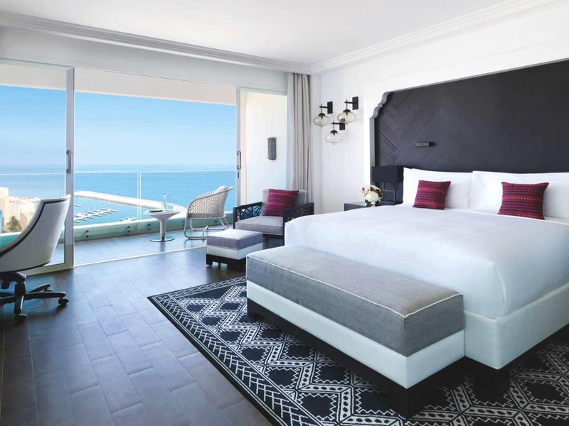 Modernes Hotelzimmer mit großem Bett und Balkon mit Meerblick.