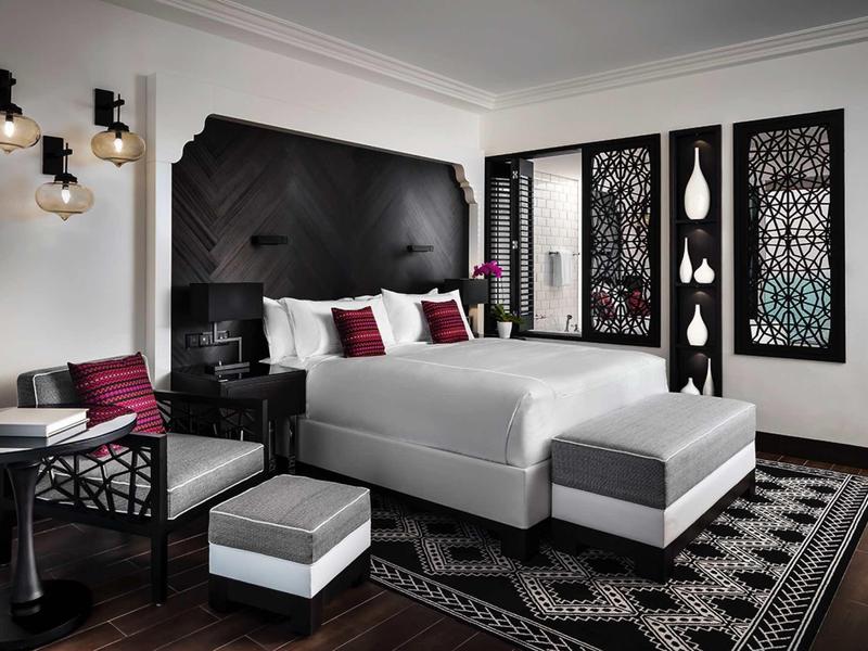 Modernes Schlafzimmer mit großem Bett, schwarzem Kopfteil, geometrischem Teppich und Wandkunst.