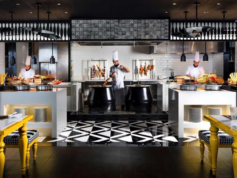 Modernes Restaurant mit zwei Köchen, schwarzen und weißen geometrischen Fliesen, gelben Stühlen.