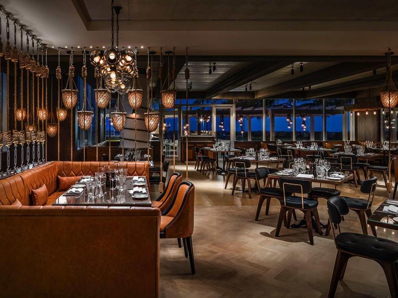 Modernes Restaurant mit warmem Licht, Holztischen, Lederbänken und stilvollen Hängelampen.