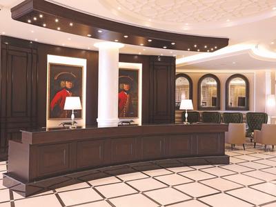 Eleganter Hotel-Empfang mit dunklem Holztresen, weißen Säulen und stilvollen Gemälden an der Wand.