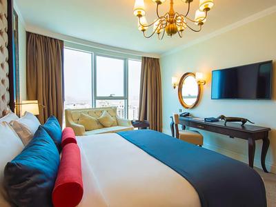 Elegantní hotelový pokoj s velkou postelí, výhledem z okna a klasickým psacím stolem.