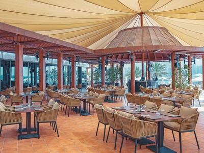 Großer, offener Restaurantbereich mit Holzsäulen, Rattanstühlen und gelbem Stoffdach in warmem Licht.