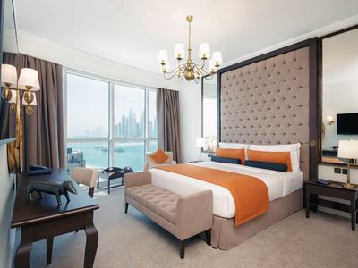 Modernes Hotelzimmer mit großem Bett, Panoramafenstern und Blick auf eine Stadt und Wasser.