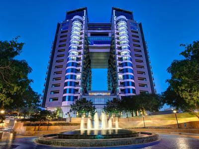 Symmetrisches Hochhaus mit blauer Beleuchtung und beleuchtetem Brunnen im Vordergrund bei Nacht.