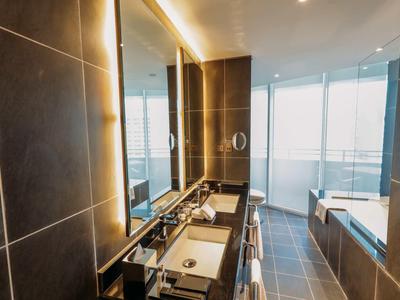 Lehátko s deštníkem u bazénu s výhledem na moderní panorama města při západu slunce.