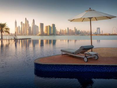 Lehátko s deštníkem u bazénu s výhledem na moderní panorama města při západu slunce.