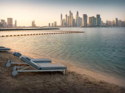 Leere Liegestühle am Strand mit Blick auf hohe Wolkenkratzer in weiter Stadt am Abend.