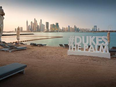 Strand mit Sonnenliegen, geschlossenen Sonnenschirmen und Dubai Skyline im Hintergrund bei Dämmerung.