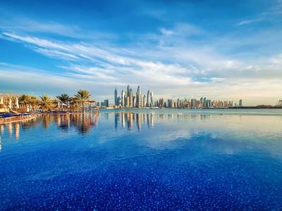 Blick auf einen ruhigen blauen Pool mit Spiegelung der Skyline und blauem Himmel im Hintergrund.