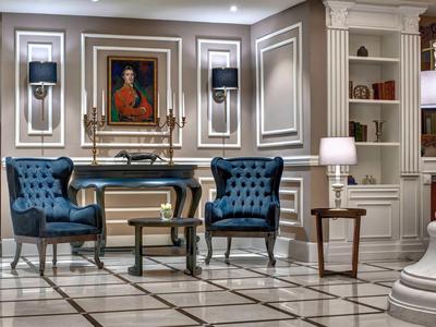 Elegantes Wohnzimmer mit blauen Samtsesseln, Marmorboden, Holzregal und klassischem Gemälde.