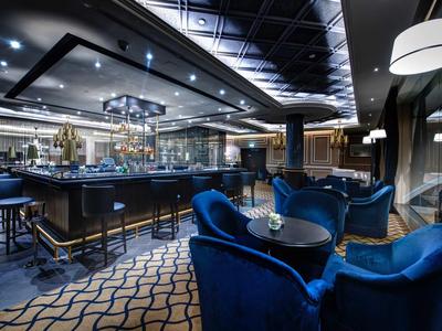 Moderní hotelový bar s modrými křesly, stoly a stylovým osvětlením.