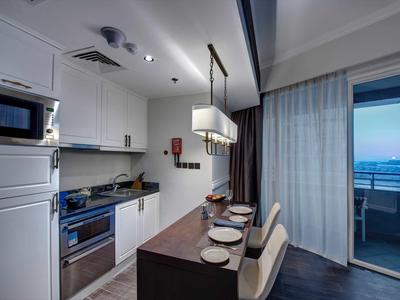 Moderne Küche mit weißer Einrichtung, Kochinsel, zwei Stühlen und Balkon mit Meeresblick bei Dämmerung.